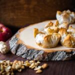 baked brie on a natural cutting board with nuts and an apple