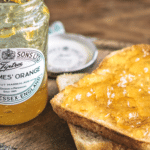 orange jelly jar next to a piece of toast with jelly on it