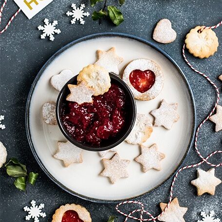 bowl of Christmas jam on a plate, surrounded by cut out shape cookies sprinkled with powdered sugar
