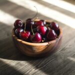 wooden bowl full of cherries on a table in the streaming sunlight