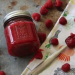 jar of raspberry jam on a tray next to fresh berries