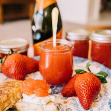 jar of strawberry-prosecco jelly surrounded by a scone, fresh berries, and a bottle of Prosecco