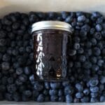 tin full of fresh blueberries with a jar of blueberry jam on top