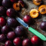 plums on a tray with a paring knife