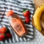 strawberries, bottle of raw honey and a banana on a striped dish towel
