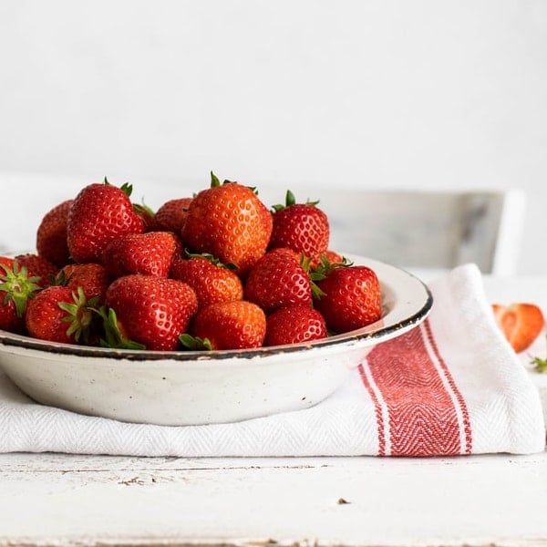 bowl of strawberries on a kitchen towel on a white table