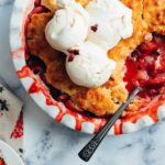 dish of fruit cobbler with a spoon in it, topped with vanilla ice cream